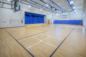 Barton Pond Elementary School Gymnasium with a Basketball Court and a Stage Behind Blue Curtains