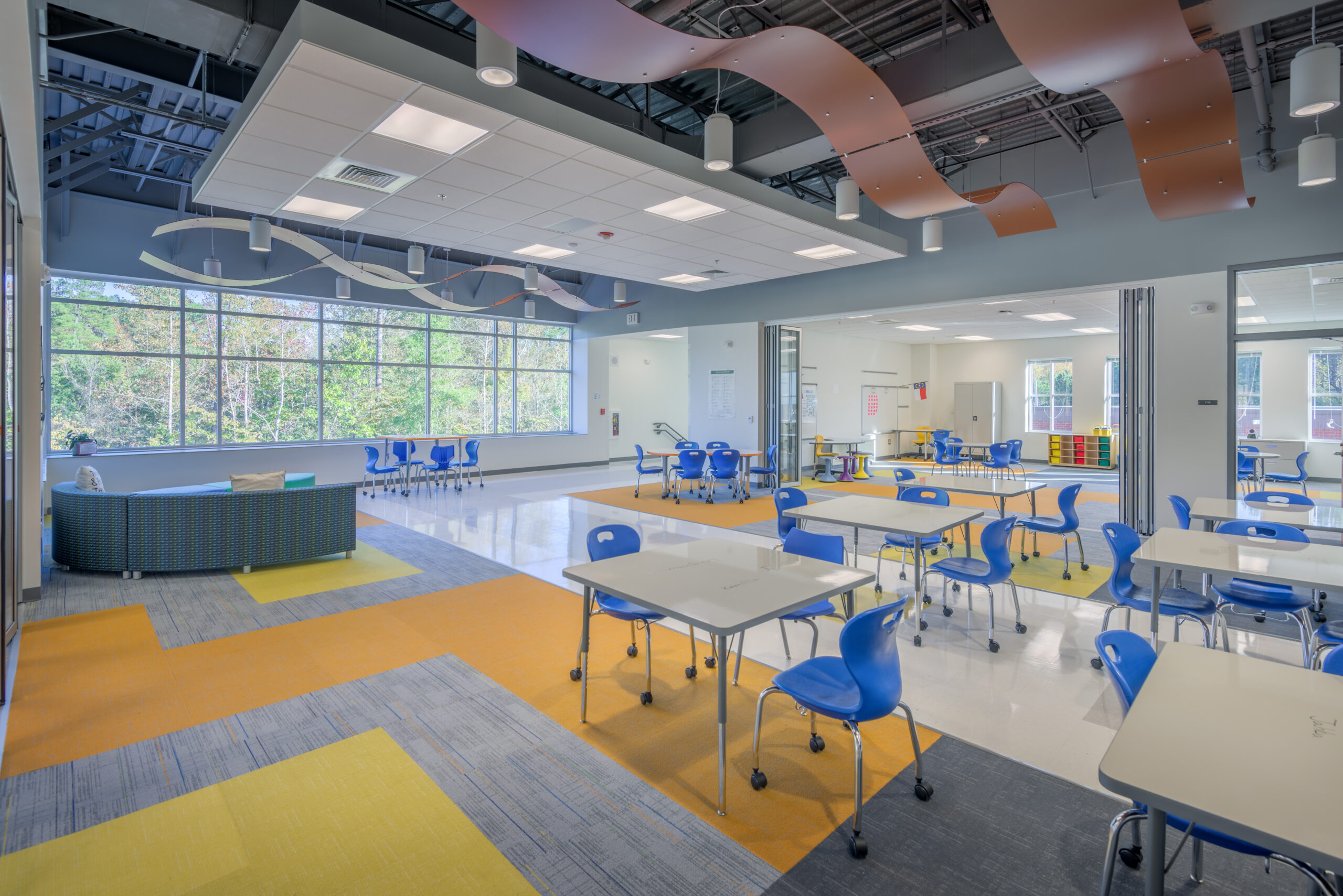 Barton Pond Elementary School Flex Space with Tables, Chairs, Transparent Room Dividers, and Decorative Ceiling Details