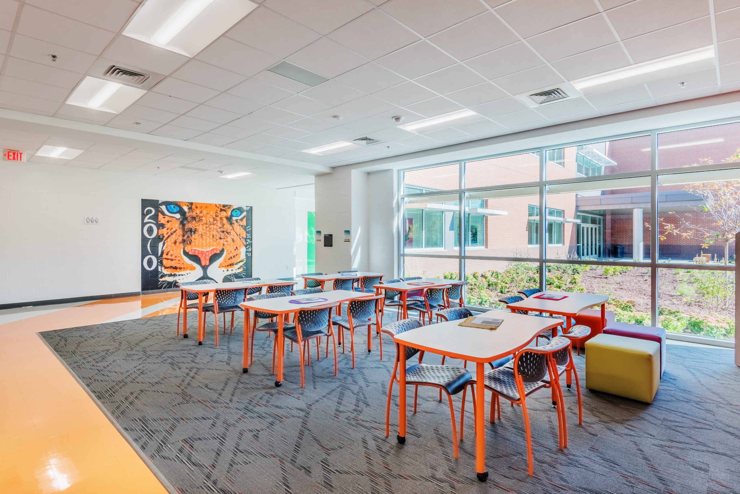 Fuquay-Varina High School Collaborative Workspace with Orange Tables and Chairs and a Bengal Painting on the Wall