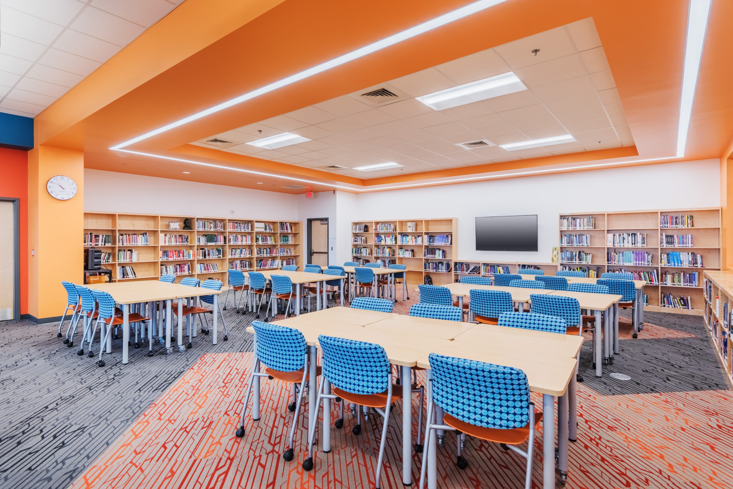 Fuquay-Varina High School Library with Full Bookshelves, Tables for Students, and a Decorative Orange Ceiling